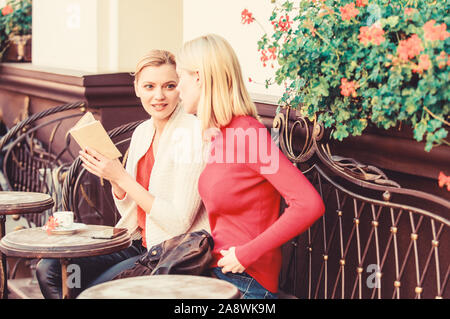 Reading inspiring book. Book every girl should read. Girls friends sitting cafe terrace drinking coffee. Female literature. Self improvement and education. Discussing popular bestseller book. Stock Photo