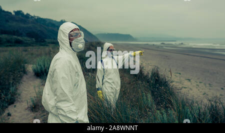 People in bacteriological protective suits watching the sea Stock Photo