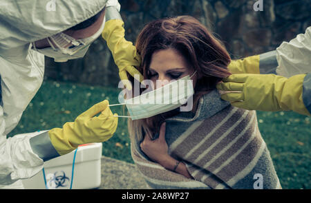 People in bacteriological protective suits putting a mask on woman Stock Photo