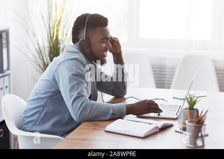 Cheerful manager wearing headset and using laptop, speaking with client Stock Photo