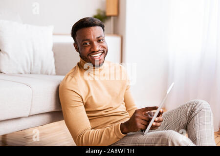 Black Guy Using Tablet Sitting On Floor At Home Stock Photo