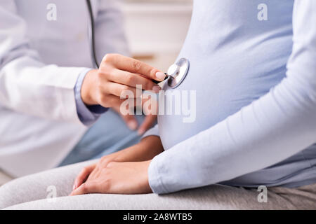 Unrecognizable Doctor Holding Stethoscope Near Pregnant Woman's Belly Indoor, Cropped Stock Photo