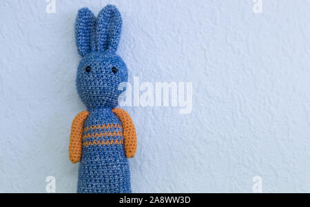 Close up on Crocheted orange and blue bunny rabbit on white textured wall background Stock Photo