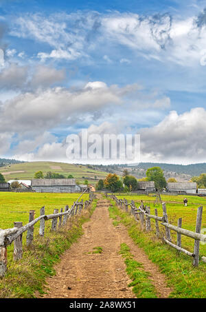 Beautiful autumn scenery in the mountains with wooden fence and dirt road. Mountain ridges on background. Carpathian Mountains. Ukraine Stock Photo