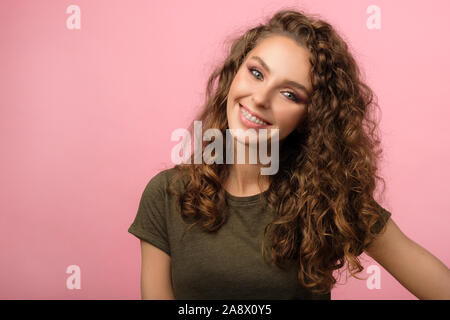Closeup portrait of attractive young female with curly hair and pretty smile wearing dental braces isolated on pink background Stock Photo