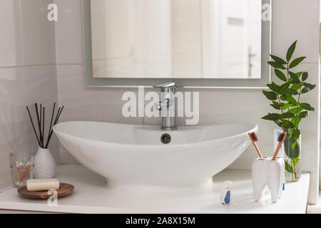 Brown bio-degradable, compostable bamboo toothbrushes in a tooth shape cup in a bathroom white interior. Green plant decor in background. Stock Photo