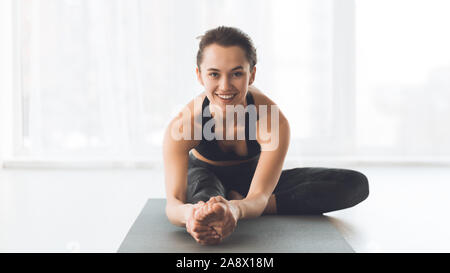 Happy fit woman stretching legs, training in light studio Stock Photo