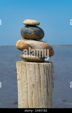A stack of colorful stones on a wooden column in front of the sea and the blue sky - mediation concept Stock Photo