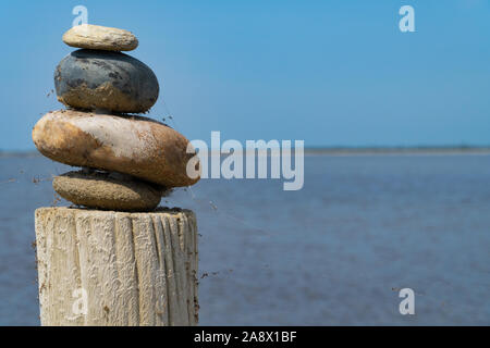 A stack of colorful stones on a wooden column in front of the sea and the blue sky - mediation concept Stock Photo