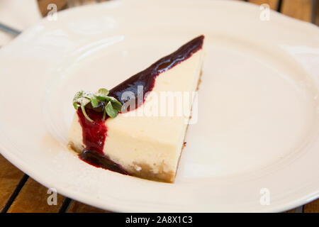 A slice of cheesecake with strawberry syrup, served in a white plate Stock Photo