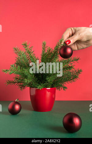 Womans hand decorates small red Christmas tree with red balls. Close up. Xmas card. Holiday winter time. Stock Photo