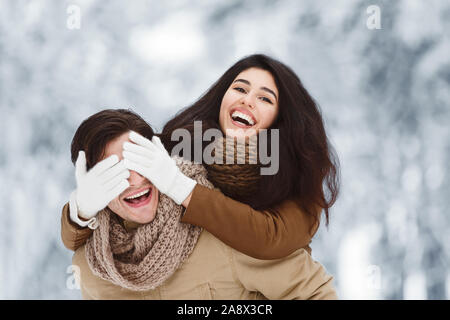 Happy Girlfriend Closing Boyfriend's Eyes Standing In Snowy Forest Stock Photo