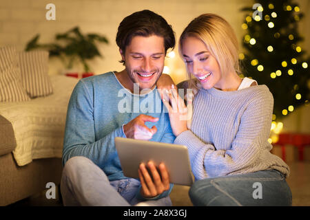 Loving couple using digital tablet next to Christmas tree Stock Photo