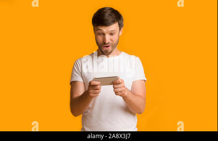 Man Playing On Smartphone Standing Over Yellow Studio Background Stock Photo