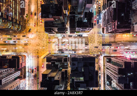 Car, taxi, and bus traffic on road intersection at night in Hong Kong downtown district, drone aerial top view. Street commuter Asia city life concept