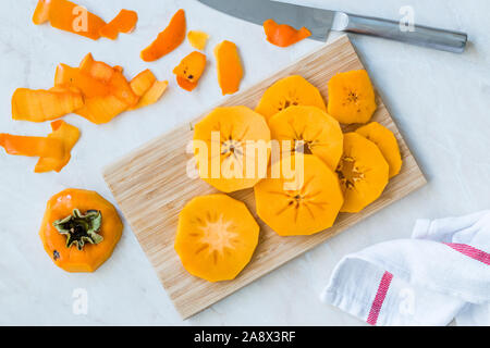 Sliced Persimmon Fruit Slices on Wooden Board with Knife. Organic Food. Stock Photo