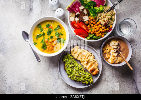 Flat lay vegan food. Chocolate smoothie bowl, Buddha bowl with tofu, chickpeas and quinoa, lentil soup and toasts on a gray background. Stock Photo
