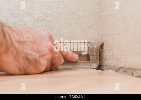 Technology installation and installation of plastic floor plinth - the master mounts the decorative cover on the plinth Stock Photo