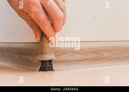 Technology of installation and installation of plastic floor plinth - Master sets the outer corner on the baseboard Stock Photo
