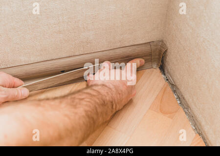 Technology installation and installation of plastic floor plinth - the master mounts the decorative cover on the plinth Stock Photo