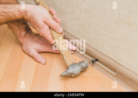 The technology of installation and installation of plastic floor plinth on a concrete or stone wall - Master hammer in a plinth dowel-nail Stock Photo