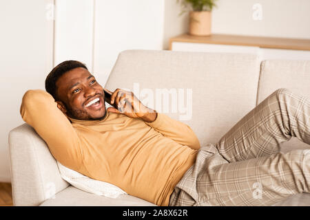 Afro Man Talking On Cellphone Lying On Couch At Home Stock Photo
