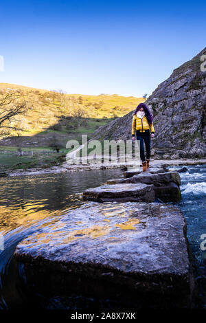 A pretty young athletic women crosses over the famous Dovedale stepping stones, keeping her balance on the icy rocks, National trust, Peak District Stock Photo