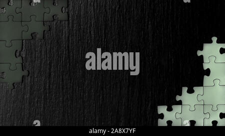 Black nd white puzzle in the corner of the image on a black natural stone background of slate. A frame with an empty space for your description. Stock Photo