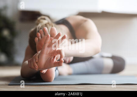 Flexible girl stretching at home, touching her knees with forehead Stock Photo