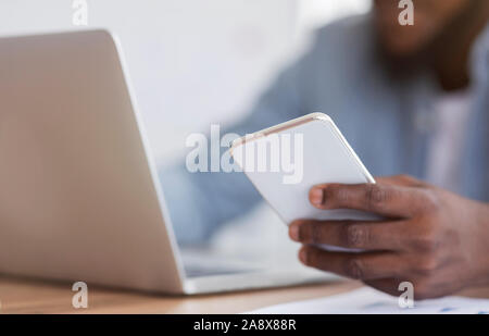 Unrecognizable black entrepreneur using smartphone and working on laptop Stock Photo