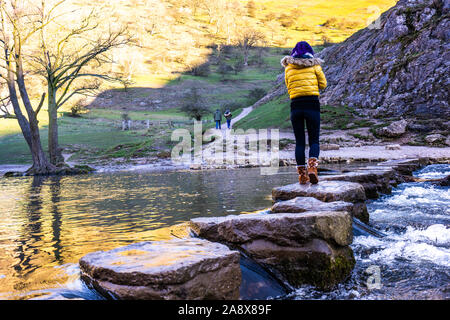 A pretty young athletic women crosses over the famous Dovedale stepping stones, keeping her balance on the icy rocks, National trust, Peak District Stock Photo