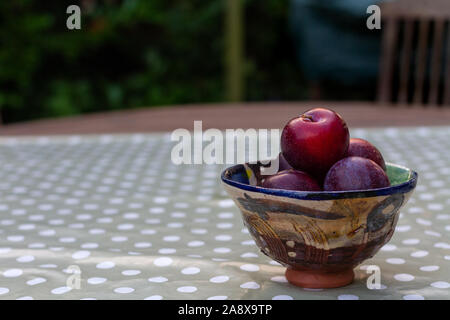 Close-up of dark red and purple plums in handmade ceramic bowl on wooden table with polka dot table cloth Stock Photo