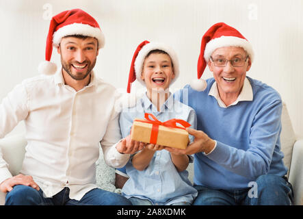 Boy, Father, Grandfather In Santa Hats Sitting On Couch Indoor Stock Photo