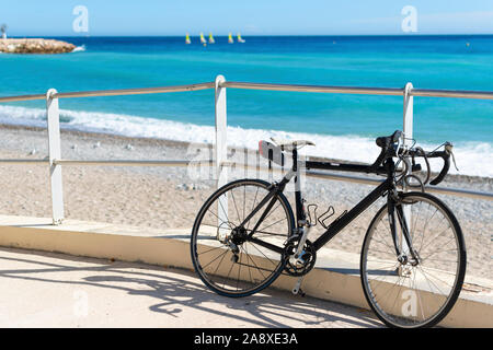 A bicycle sits parked along a ramp to the beach as a group of matching sailboats are blurred in the distance on the French Riviera in Menton, France Stock Photo