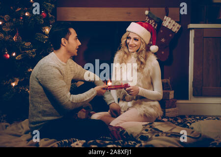 Loving couple by a roaring log fire at Christmas pulling a cracker Stock Photo