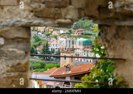 View of the Medieval Church of Saint Anthony clock tower and city of Dolceacqua, Italy, from a window in a stone wall on the ancient hilltop castle. Stock Photo