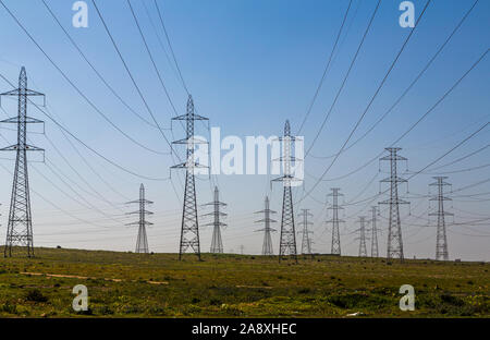 Panorama of electricity pylons, electric power transmission masts, spread out across a green landscape against a blue sky background, Morocco Stock Photo