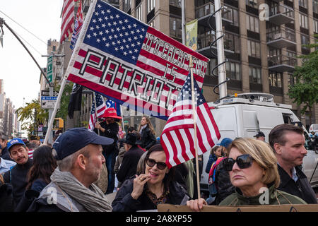 New York, NY, USA. 11th Nov, 2019. New York City's Veterans Day Parade, today marking the 100th anniversary of the armistice ending the fighting of the first World War, was attended by a number of people protesting President Trump, who spoke at the opening ceremony, and a smaller number of pro-Trump supporters. Here a large American flag is overprinted with 'Impeachment is Patriotic' Credit: Ed Lefkowicz/Alamy Live News Stock Photo