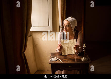 Vermeer style portrait of a young maid in renaissance costume reading a letter at her window Stock Photo