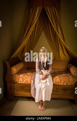 Vermeer style portrait of a young maid in renaissance costume sitting on an antique bed with her embroidery work Stock Photo