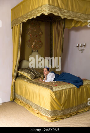 Dutch Master style portrait of a beautiful young woman in authentic renaissance costume lying on a luxury antique canopy bed in a golden bedroom of a Stock Photo