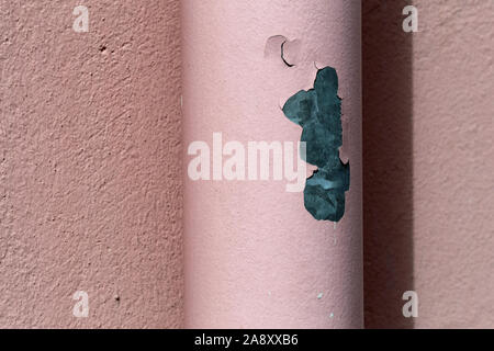Cute old rosa / pink colored painted wall and same colored metal water pipe. This is an exterior of an old, weathered building - the paint is chapped Stock Photo