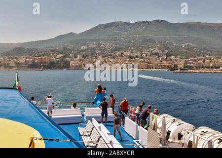 BASTIA, CORSICA, FRANCE - JULY 23, 2019: Passengers travel on the deck of Moby Vincent ferry passenger ship, cityscape in the background. Moby is an I Stock Photo