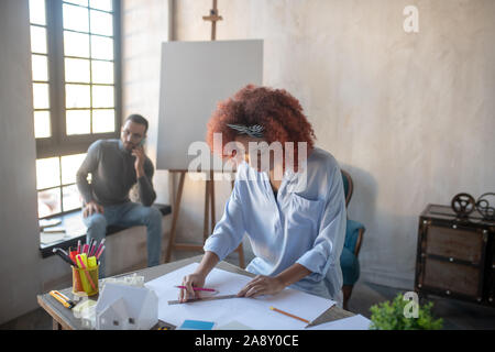Curly interior designer making sketches in spacious office Stock Photo