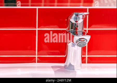Chrome water tap on a red ceramic tile background. Stock Photo
