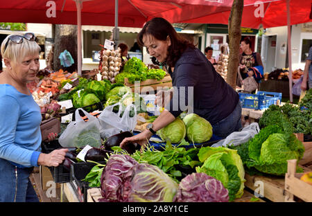 Woman selling fresh greens in fruit and vegetable stall at outdoor covered market,  Pula, Croatia Stock Photo