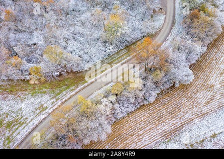 WIndy gravel road through forest and harvested corn field dusted by early snow, aerial view of Honey Creek Conservation Area in western Missouri Stock Photo