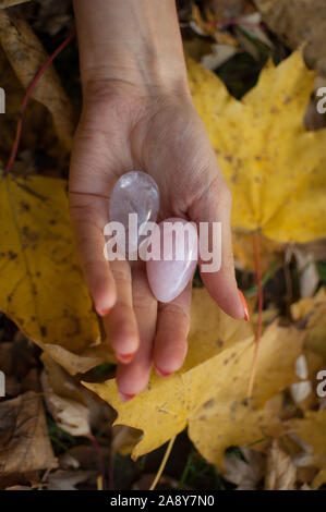 Female hands with orange manicure holding two yoni eggs made from pink quartz and transparent violet amethyst for vumfit, imbuilding or meditation on Stock Photo