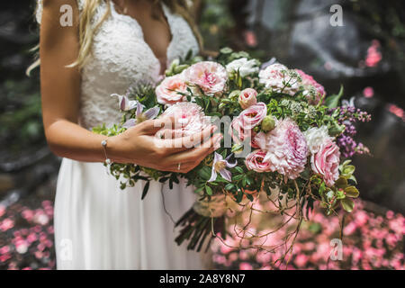 Woman holding in hands big wedding bouquet in rustic style. Greens, pink and white roses, coral chrysanthemum, peony. Pastel colored. Stock Photo