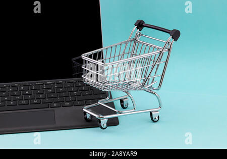 Internet shopping concept of a laptop computer with a mini shopping cart basket resting on the keyboard isolated against an blue background Stock Photo